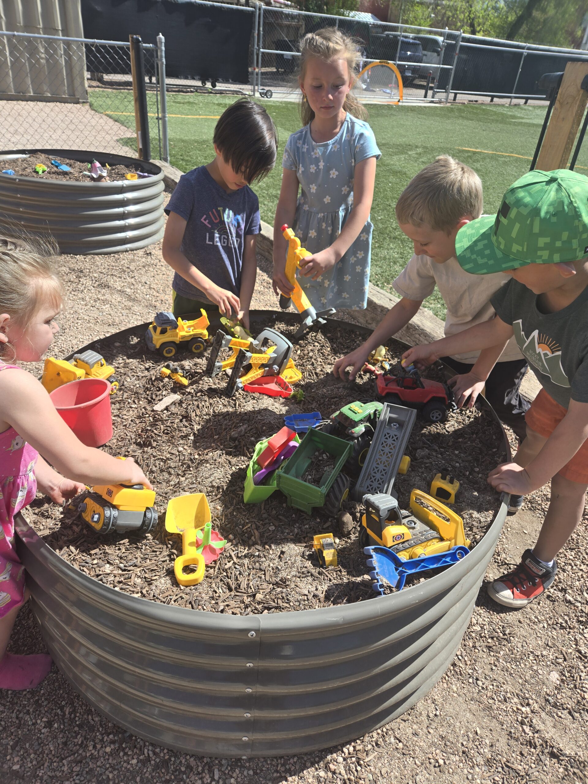 small group of children playing in a raised gardenbed with toys